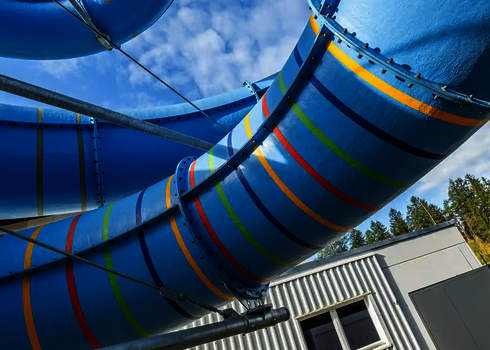 Blick von unten auf eine blaue Wasserrutsche mit bunten Streifen.