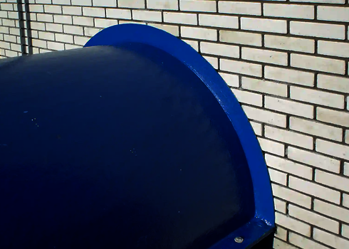 Blaue Wasserrutsche verlässt das Gebäude durch eine weiße Backsteinwand.