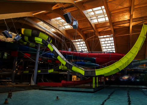 Große gelbe Boomerang Wasserrutsche in einem Hallenbad, im Hintergrund weitere bunte Wasserrutschen.