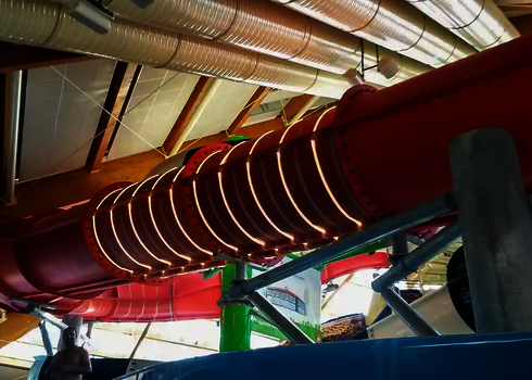 Rote Röhrenrutsche mit ringförmigen LED-Lichtern im Innenbereich eines Schwimmbads.