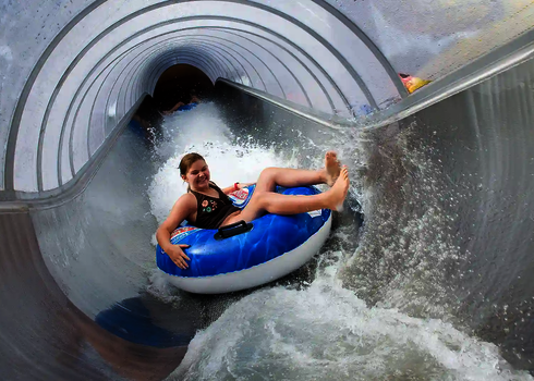 Ein Mädchen rutscht lachend auf einem blauen Reifen durch den geschlossenen Kanal des Speed Blaster.