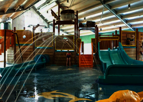 Schiffähnlicher Kinderbereich mit Wasserrutschen und Wasserspielen in einem Hallenbad.