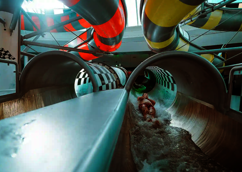 Person rutscht durch Body Racer Wasserrutsche mit Schachbrettmuster ins Wasser.