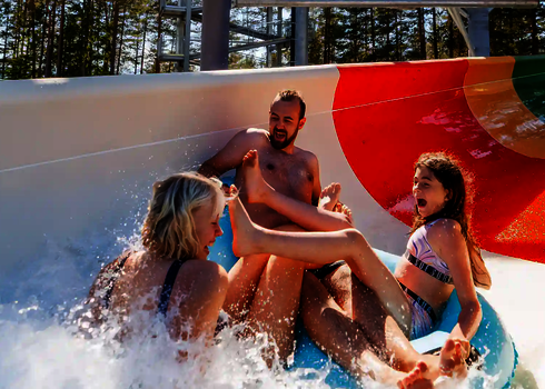 Familie auf einem blauen Rutschreifen fährt durch den offenen bunten Bereich des Family Twister