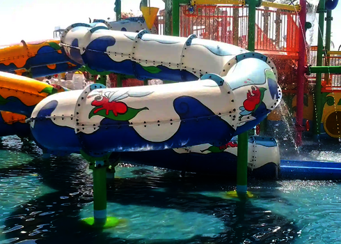 Weiß-blaue RR900-Kids vor bunter Wasserspielstruktur in einem Poolbecken.