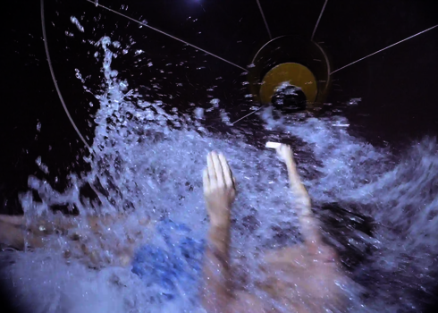 Person rutscht in der Wasserrutsche durch Wasserwirbel auf den Auslauf zu.