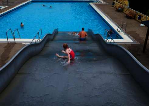 Sicht von oben, wie ein Kind in Badebekleidung eine Breitwellenrutsche herunterruscht.
