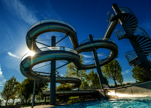 Sonnenlicht fällt durch verschlungene Edelstahlrutschen, die in ein Becken führen.