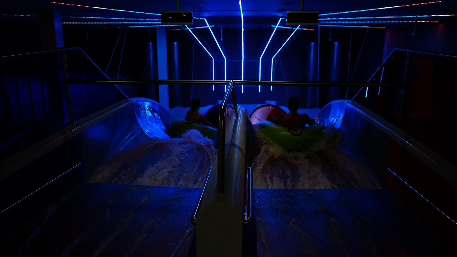 Zwei Personen auf grünen Reifen rutschen gleichzeitig in die Raft Racer Reifenrutsche bei LED-Licht.