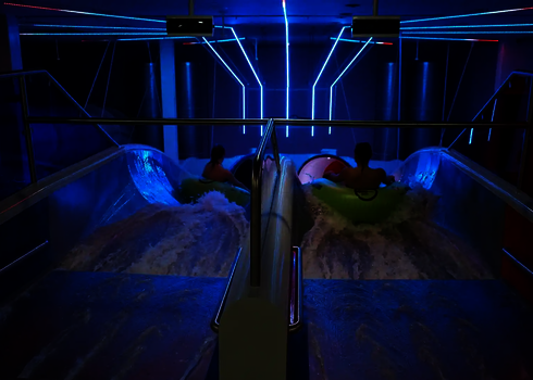 Zwei Personen auf grünen Reifen rutschen gleichzeitig in die Raft Racer Reifenrutsche bei LED-Licht.