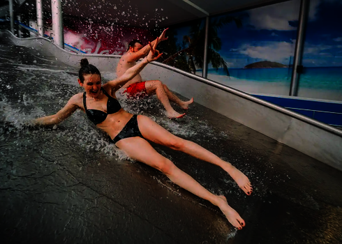 Zwei Personen rutschen auf einer Edelstahl Breitwellenrutsche und lachen dabei.