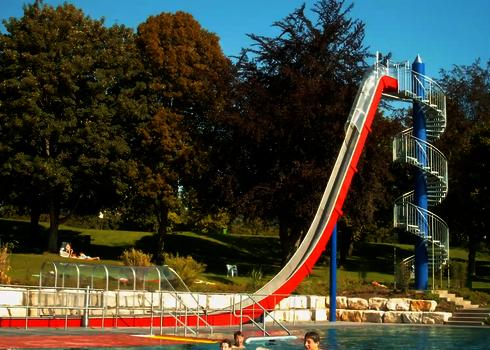Freifallrutsche mit rot-weißem Design mündet in einem Auslaufbecken, in einem Freibad mit Schwimmern.