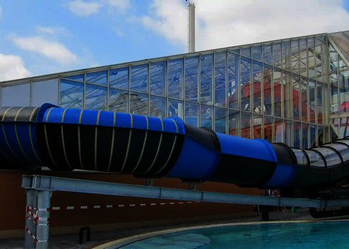 Blau-schwarze Family Twister Wasserrutsche endet über einem Außenbecken.