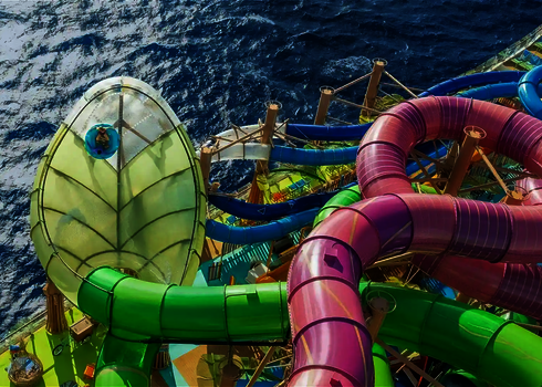 Person fährt auf blauem Rutschreifen die grüne Lotus Wasserrutsche über dem Meer.