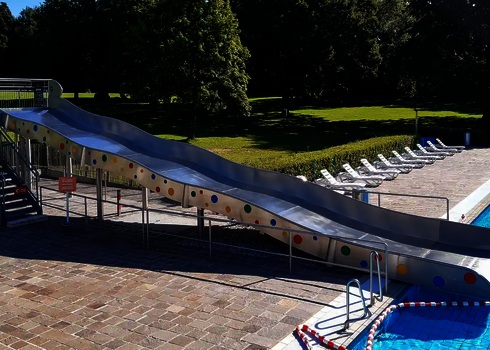 Seitenansicht auf eine Breitwellenrutsche mit bunten Punkten in einem Freibad.