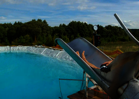 Blick von Hinten auf einen Cannonball in dem eine Person sitzt, mit Blick auf ein türkisfarbenes Schwimmbecken.