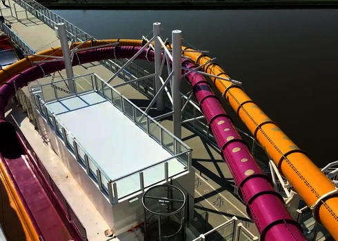 Zwei Wasserrutschen in Pink und Gelb verlaufen nebeneinander auf einem Schiff.