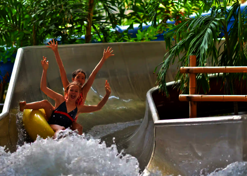 Kinder rutschen lachend und mit erhobenen Händen den Crazy River.