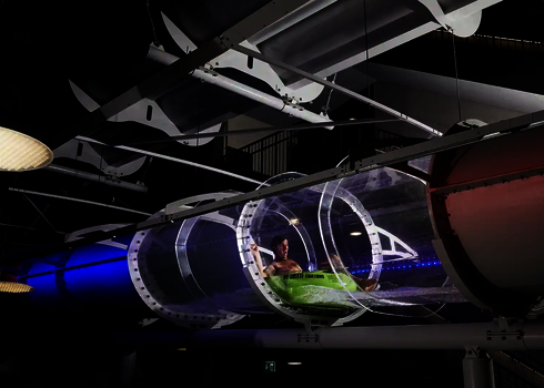 Gesamtansicht einer beleuchteten Acryl-Röhre mit rutschendem Mann auf Reifen in dunkler Indoor-Umgebung.