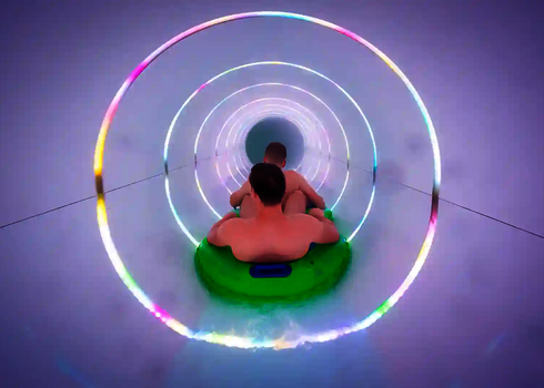 Zwei Personen auf einem Reifen im LED-beleuchteten Rutschentunnel mit Lichtkreisen.
