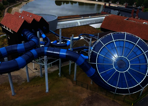 Seitenansicht des Cyclone-Trichters in Blau mit Röhrenrutsche, Gebäuden und See im Hintergrund.