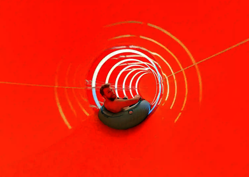 Eine orangene Wasserrutsche von innen, mit einem Mann auf einem blauen Rutschreifen.