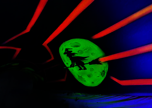 Hexensilhouette vor grünem Mond, leuchtend im Schwarzlicht einer Wasserrutsche.