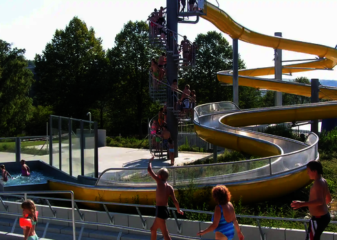 Kinder warten auf gelber Rutsche, andere plantschen im Wasserbecken.