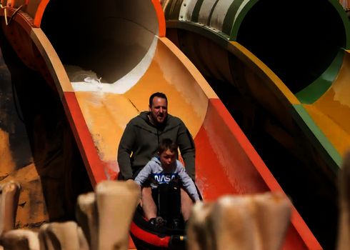 Ein Mann und ein Kind rutschen gemeinsam aus der Tunnelöffnung einer Harakiri Freizeitparkrrutsche.