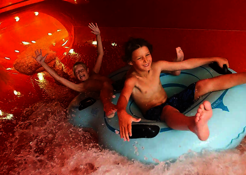 Zwei Kinder rutschen lachend auf hellblauen Rutschreifen im überdachten Family Twister.