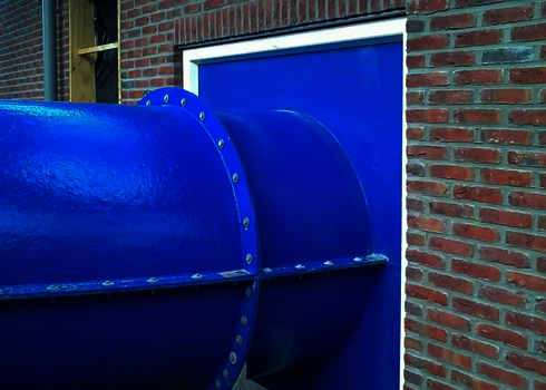 Nahaufnahme einer blauen Wasserrutsche beim Eintritt in die Wandöffnung eines Gebäudes.