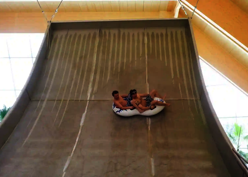 Zwei Personen auf einem Doppelreifen rutschen die fast senkrechte Boomerang-Wand hinab.