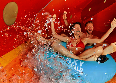 Paar rutscht lachend auf blauem Reifen durch den Family Twister, spritzendes Wasser.