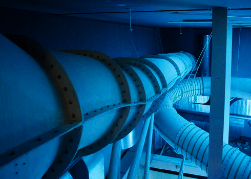 Röhrenrutsche in blauem Licht, die unter der Decke eines Hallenbads entlangführt.