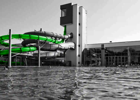 Außenansicht eines Bads mit grüner und silberner Wasserrutsche am Rutschenturm.