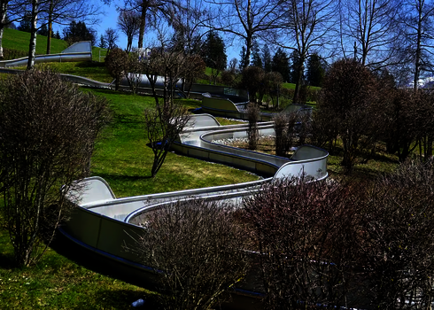 Edelstahl-Wasserrutsche schlängelt sich durch hügelige Landschaft mit kahlen Sträuchern.