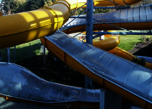 Gelbe Wasserrutsche, teils mit transparenter Überdachung, getragen von Stahlstützen.