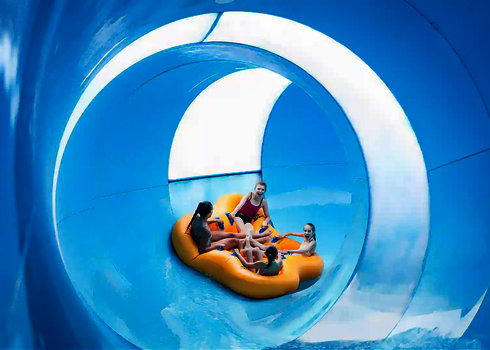 Innenansicht einer großen blauen Wasserrutsche mit vier Personen in einem gelben Rutschreifen.