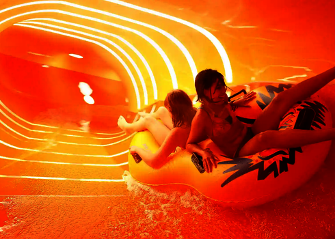 Eine gelbe Wasserrutsche von innen, mit zwei Kindern auf einem gelben Rutschreifen.