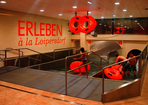 Mehrere Personen mit orangenen Rutschreifen kommen im Auslauf einer Wasserrutsche in der Therme Loipersdorf an.