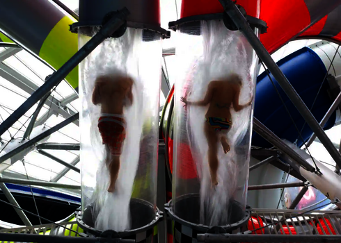 Zwei Personen rutschen gleichzeitig in den transparenten Acryl Abschnitt der Body Racer Wasserrutsche.