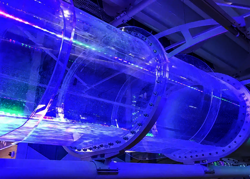 Transparenter Rutschentunnel mit LED-Lichteffekt in Violett- und Grüntönen in einer Indoor-Anlage.