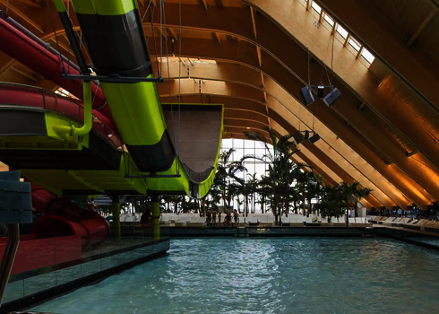 Boomerang-Rutsche über einem Wellenbecken mit Liegen, Palmen und Tageslichtkuppel.