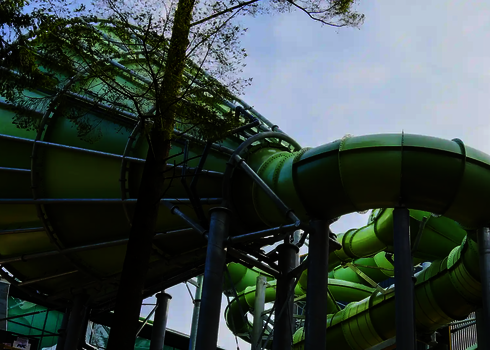 Ein grüner Cyclone-Trichter mit angrenzender Röhrenrutsche auf Stahlstützen zwischen Bäumen.