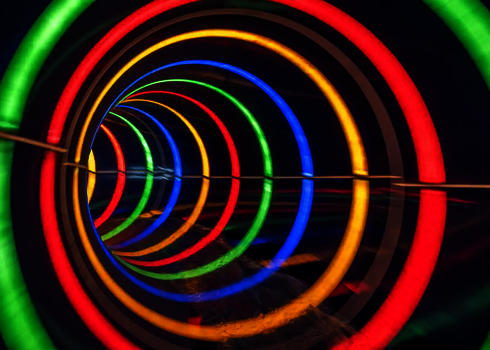 Innenansicht einer dunklen Röhrenrutsche mit bunt gestreiften Tageslichteffekten.