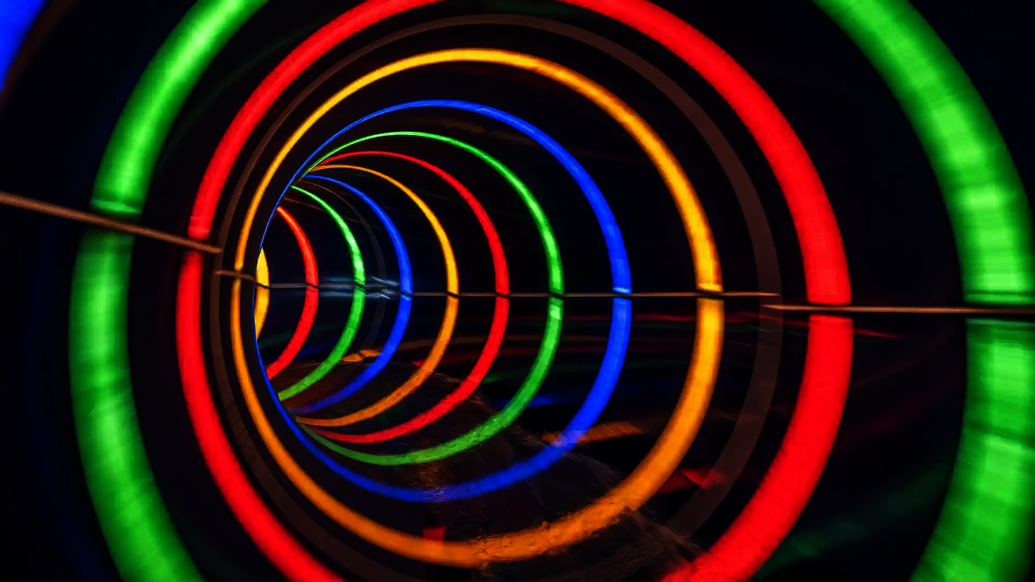 Innenansicht einer dunklen Röhrenrutsche mit bunt gestreiften Tageslichteffekten.