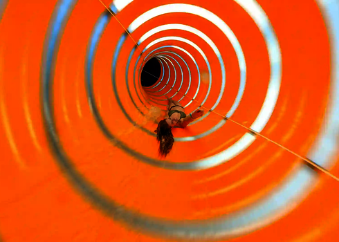 Eine orangene Wasserrutsche von innen, mit einer Frau, die rücklings rutscht.