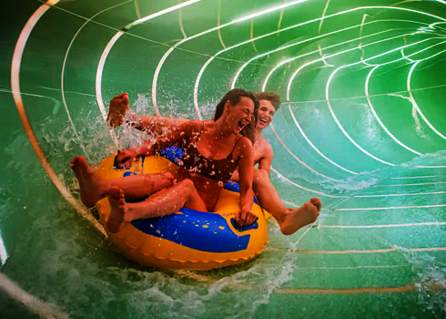 Eine grüne Wasserrutsche von innen, mit zwei Personen auf einem gelben Rutschreifen.