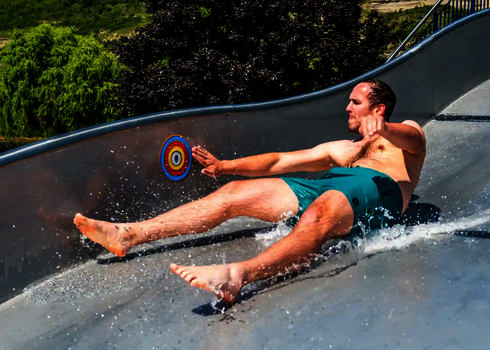 Ein Mann in Badebekleidung auf einer Breitwellenrutsche mit buntem Interactivity Button.