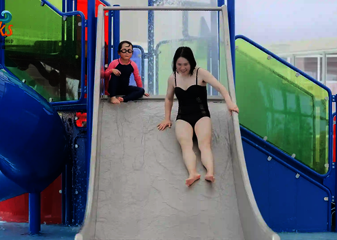 Frau rutscht eine Kinderrutsche, Kind sitzt daneben.